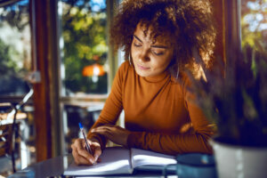 Portrait of student with curly hair and in turtleneck sitting in cafe and studying for exams.