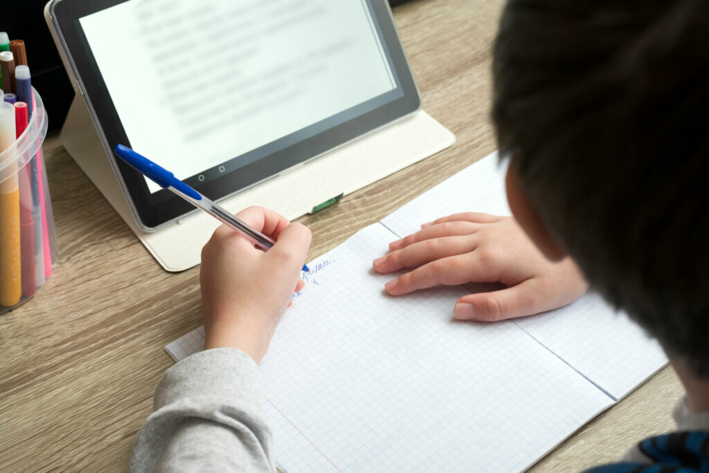 Close up boy studying at home with tablet and doing school homework. Distance learning online education or stay at home concept. Soft focus.