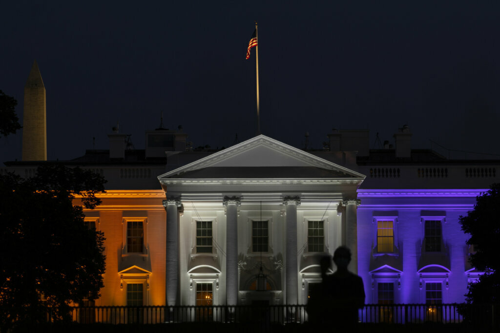 A person is silhouetted against the White House lit in purple and gold to mark the 100th anniversary of women's suffrage during the third night of the Republican National Convention in Washington, Wednesday, Aug. 26, 2020. (AP Photo/Carolyn Kaster)