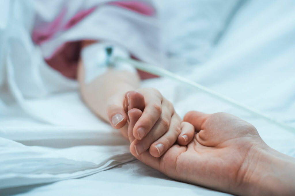 Recovering Little Child Lying in the Hospital Bed Sleeping, Mother Holds Her Hand Comforting. Focus on the Hands. Emotional Family Moment.