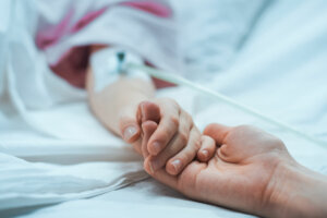 Recovering Little Child Lying in the Hospital Bed Sleeping, Mother Holds Her Hand Comforting. Focus on the Hands. Emotional Family Moment.