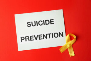 Paper sheet with text SUICIDE PREVENTION and yellow ribbon on color background