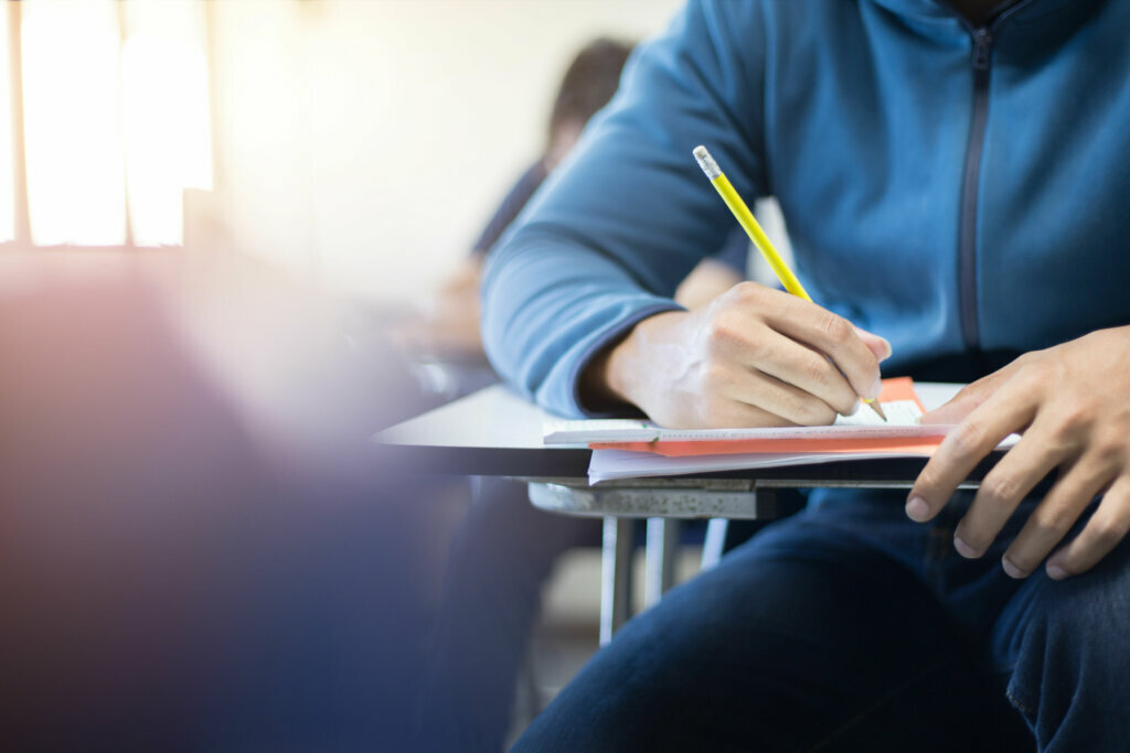 School student man hand writing by marking choices on answer sheet paper for final examination test in classroom concept