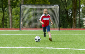 School kid with mask and soccer ball in a physical education lesson. Safe back to school during pandemic concept. Social distancing to fight COVID