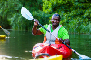 Black man paddling with canoe on forest river