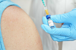 Hand in blue gloves holding syringe and chloroquine phosphate (generic name, sticker own design dummy data), about to inject it to shoulder of patient near. Potential coronavirus cure concept