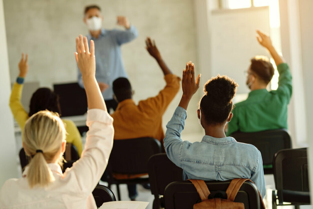 Back view of group of students raising their arms during a class at lecture hall.