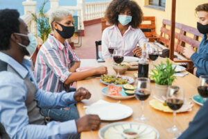 Young multiracial people eating and drinking together while wearing face protective masks Focus on black girl