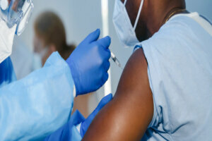 Hand of medical staff in blue glove injecting coronavirus covid 19 vaccine in vaccine syringe to arm muscle of african american man for coronavirus covid 19 immunization