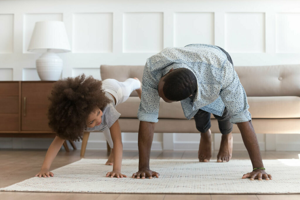 Father and small daughter in casual clothes do pushup pressup exercise on carpet on warm floor in living room.