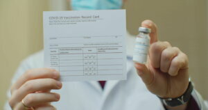 Doctor is holding a vaccination record card and corona virus vaccine vials. Passport of immunity to the coronavirus in the hands of a male doctor. Health passport as proof of recovery from COVID 19.