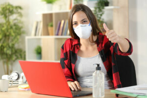 Student with mask due covid 19 gesturing thumbs up at home