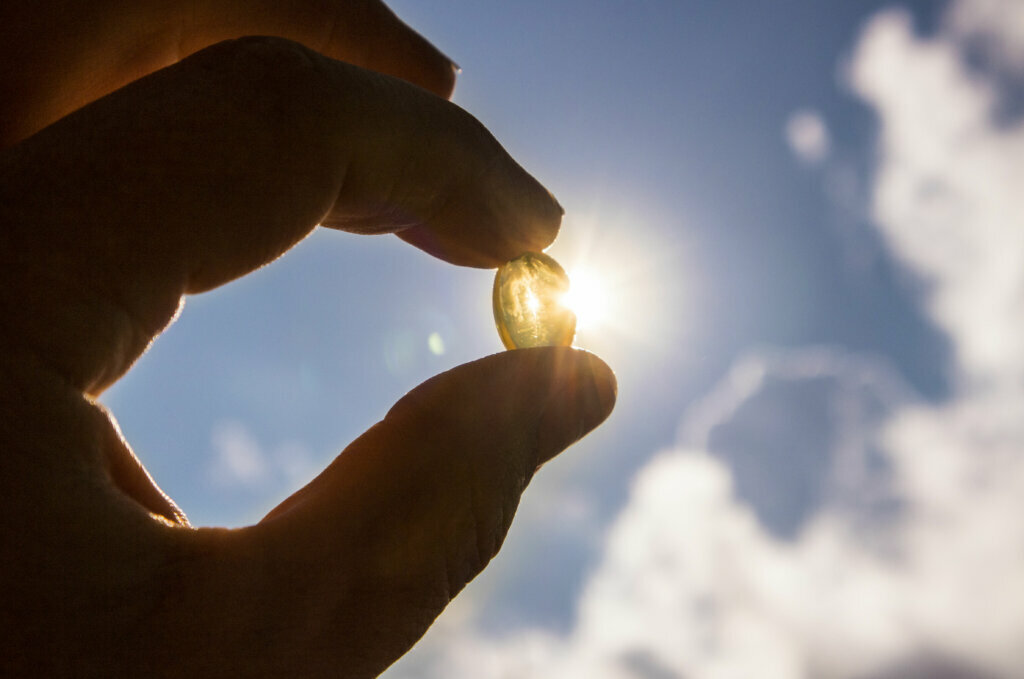 Vitamin D keeps you healthy while lack of sun. Yellow soft shell D vitamin capsule against sun and blue sky on sunny day. Cure concept.