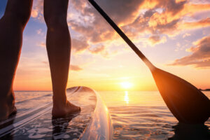Paddle boarding or standup paddleboarding on quiet sea at sunset with beautiful colors during warm summer beach vacation holiday