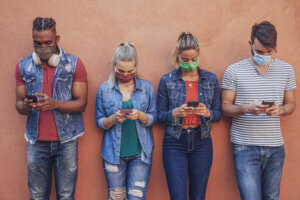 Group of people using their smartphones in covid 19 times protected with face mask Friends checking online news while standing by the wall and holding cellphones