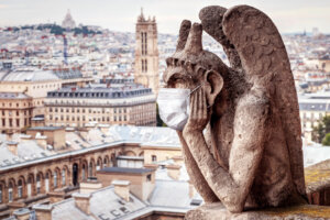 COVID 19 coronavirus in France, medical mask on gargoyle of Notre Dame in Paris. Tourist landmarks closed due to corona virus outbreak.