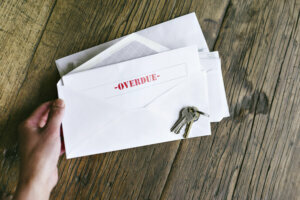Overdue Notiice in an Open Envelope with Keys on a Wood Table Hands of a Woman Holding Late Bills Rent Mortgage