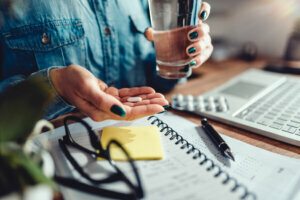 Woman sitting by the office desk and taking medical pills