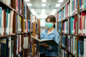 Asian university student girl wearing face protective medical mask for protection from virus disease reading book at library. Education, high school, university, learning and people concept