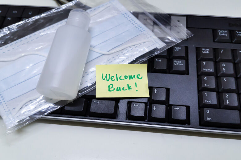 Welcome back note with hand sanitizer and mask on top of keyboard