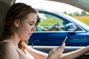 A young woman drives a car and writes an sms
