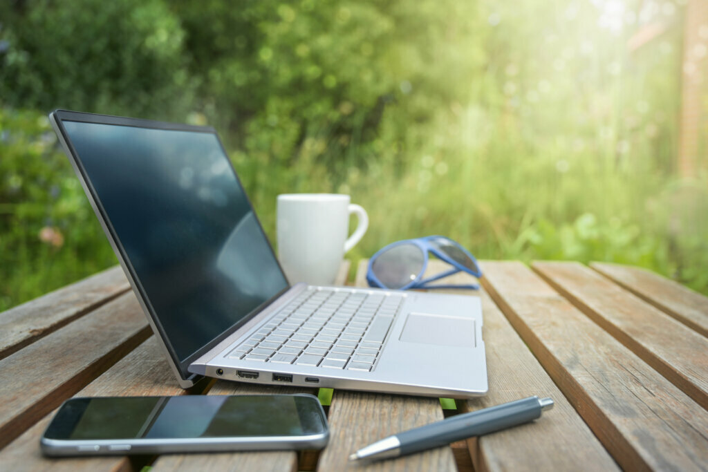 Garden office with laptop, smart phone, glasses and coffee on a wooden table in the backyard, stay home during corona crisis, copy space, selected focus
