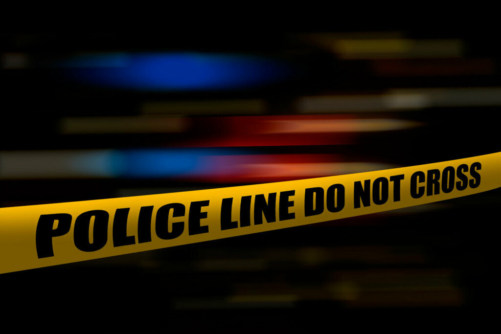 Yellow police tape at night with blurred blue and red lights from police cars and emergency vehicles.