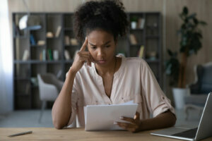 Unhappy young african american woman looking through paper document.