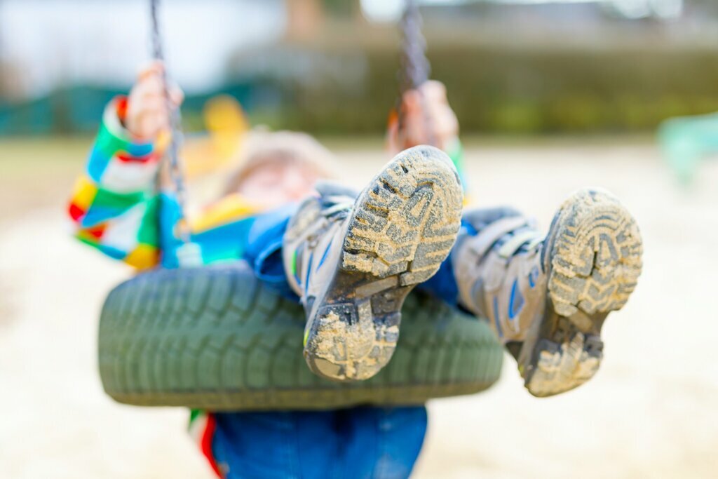 Funny kid boy having fun with chain swing on outdoor playground. child swinging on warm sunny spring or autumn day. Active leisure with kids. Selective focus, no face of kid.