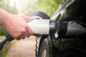 Mans hand inserting charger plug into electric car in green environment background. New energy vehicle, NEV is being loaded with electricity power. Ecology, modern day cars