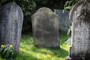 Blank gravestone in graveyard. Old, decayed and grunge, ready for text. Trees and bushes in background.