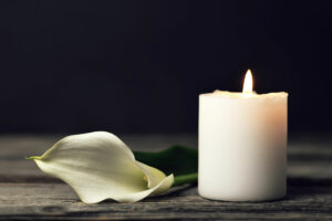 Burning candle and white calla on dark background with copy space. Sympathy card