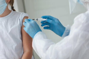 A doctor in a protective suit makes the child in a medical mask a shoulder shot . Coronavirus vaccination. Covid 19 vaccine. Doctor vaccinating child. Kids at clinic. Little girl getting flu shot.