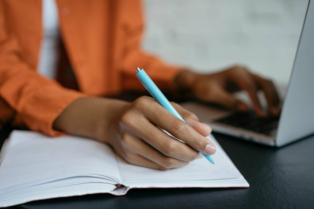 Close up shot of student hand holding pen and writing in notebook, working at home. E learning
