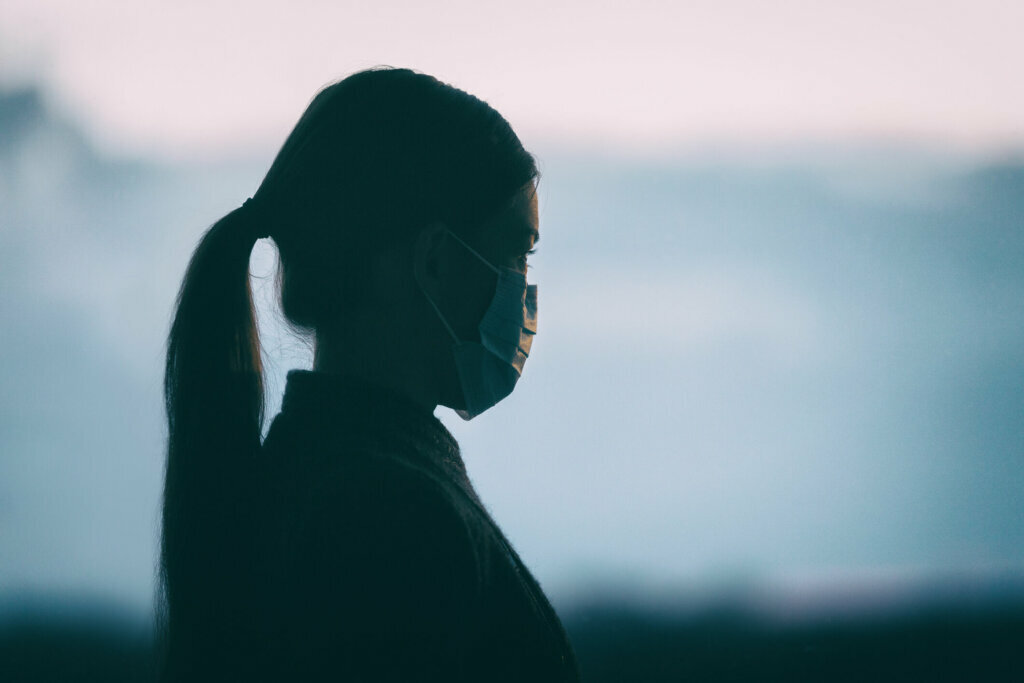 Coronavirus COVID 19 anxiety mental health problem sad woman wearing protective medical face mask silhouette alone thinking of the depressive future of society