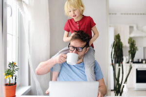 Man working from home with laptop during quarantine. Home office and parenthood at same time. Exhausted parent with hyperactive child.
