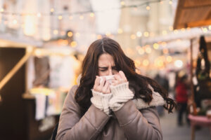 Woman blowing nose while standing on the street on cold weather.