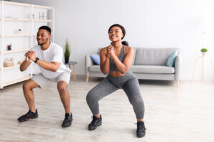 Strength workout concept. Fit black woman and her boyfriend doing squats together at home, panorama