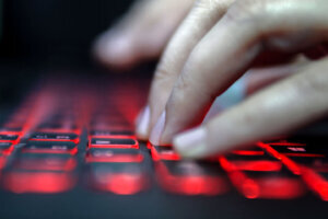 Teenage Hacker Girl Attacks Corporate Servers in Dark, Typing on Red Lit Laptop Keyboard. Room is Dark