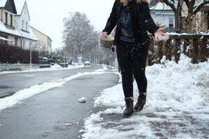 Young Millenial woman spreading salt on icy sidewalk in front of her house