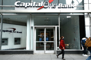 A woman wearing a face mask walks past the Capital One Bank