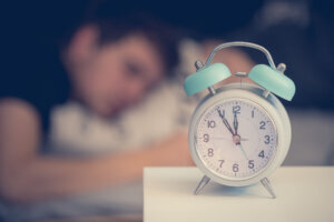 Alarm clock in the morning. Young man sleeps in the blurry background.
