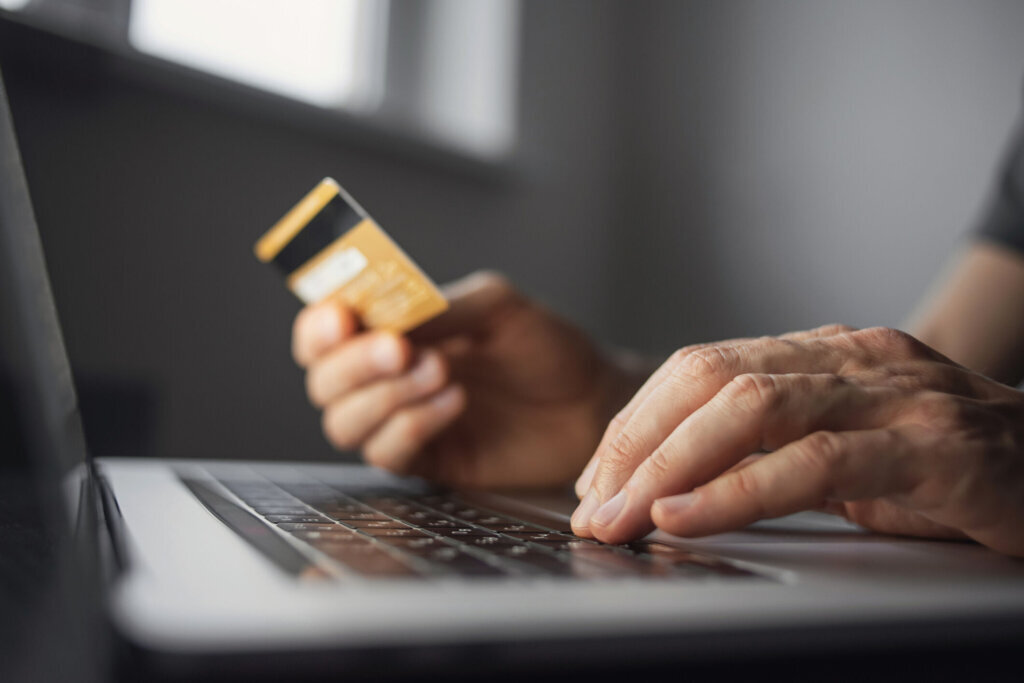 Shopping online. Young man using laptop with credit card at home