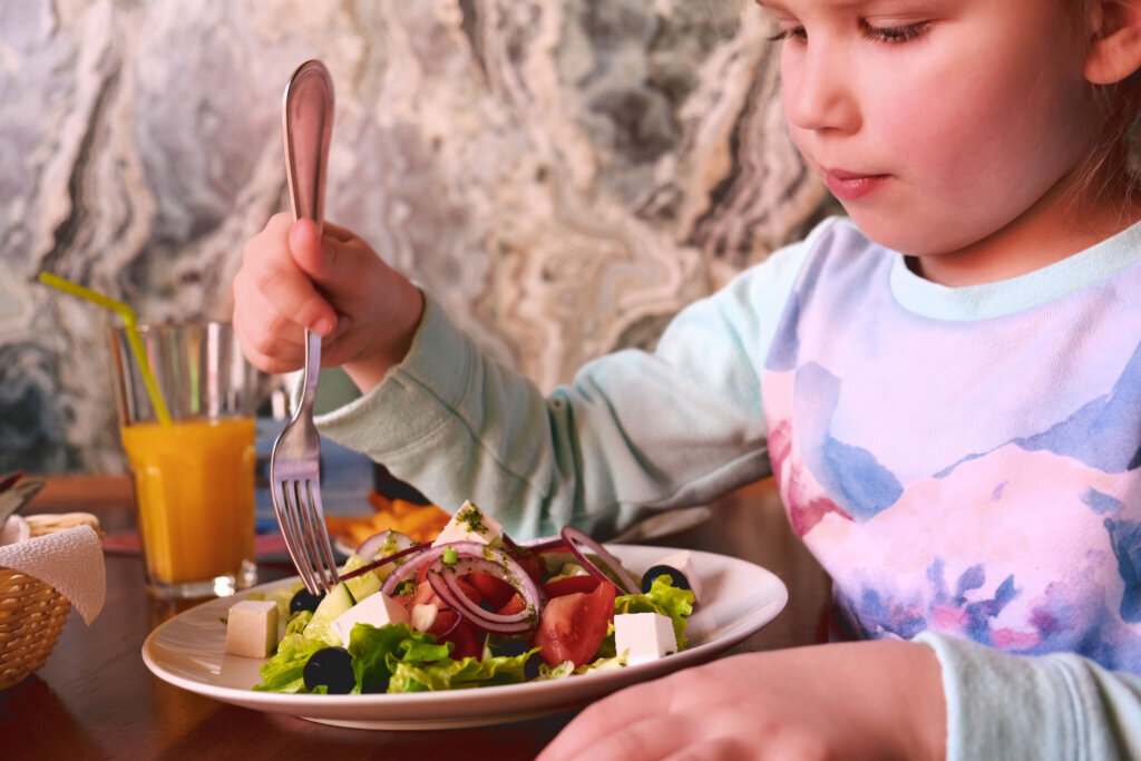 Child eating greek salad in cafe