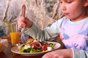 Child eating greek salad in cafe