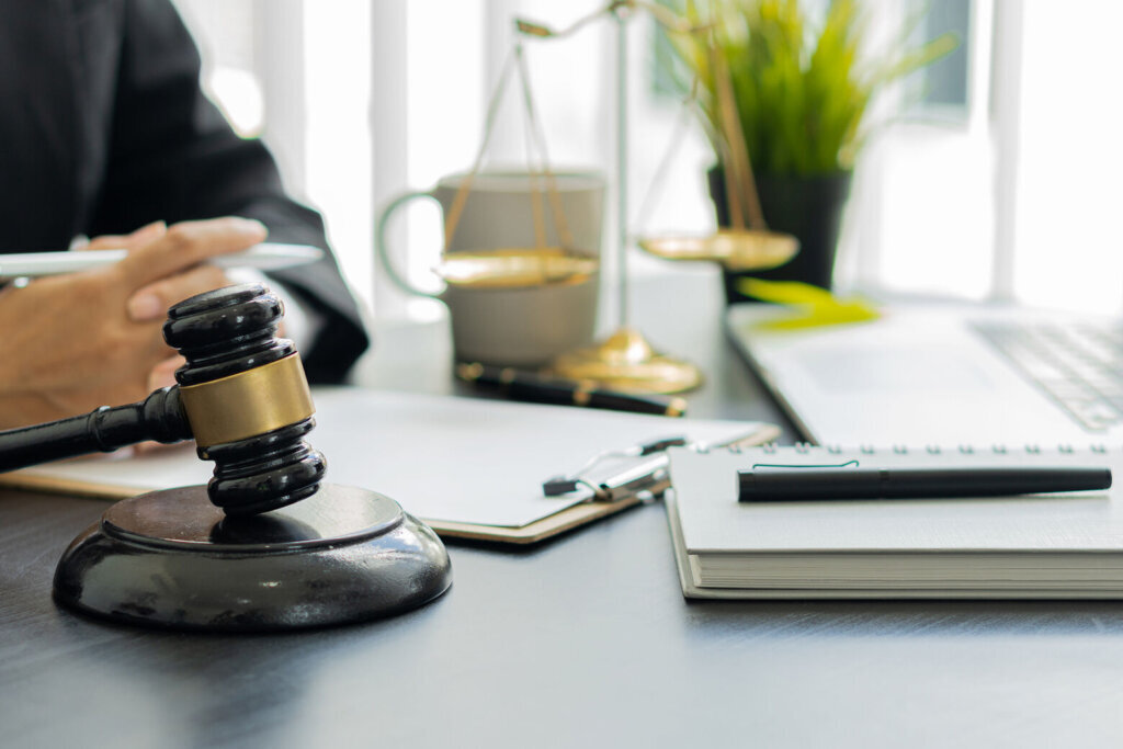 The judge's hammer is placed in front of him and the lawyer works in the office with his laptop and the scales of justice.