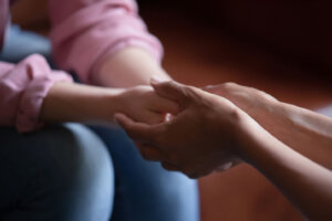 Biracial female psychologist hands holding palms of millennial woman patient