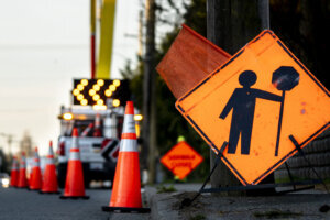 Lane closure on a busy road due to maintenance signs detour traffic temporary street work orange lighted arrow, barrels, and cones.