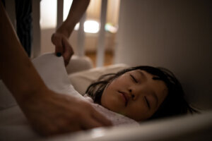 Close up asian mother tuck the blanket on kid sleep in bed.
