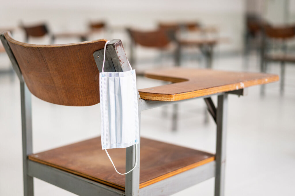 A used medical facemask hangs on a wood lecture chair in the empty classroom during the COVID 19 pandemic
